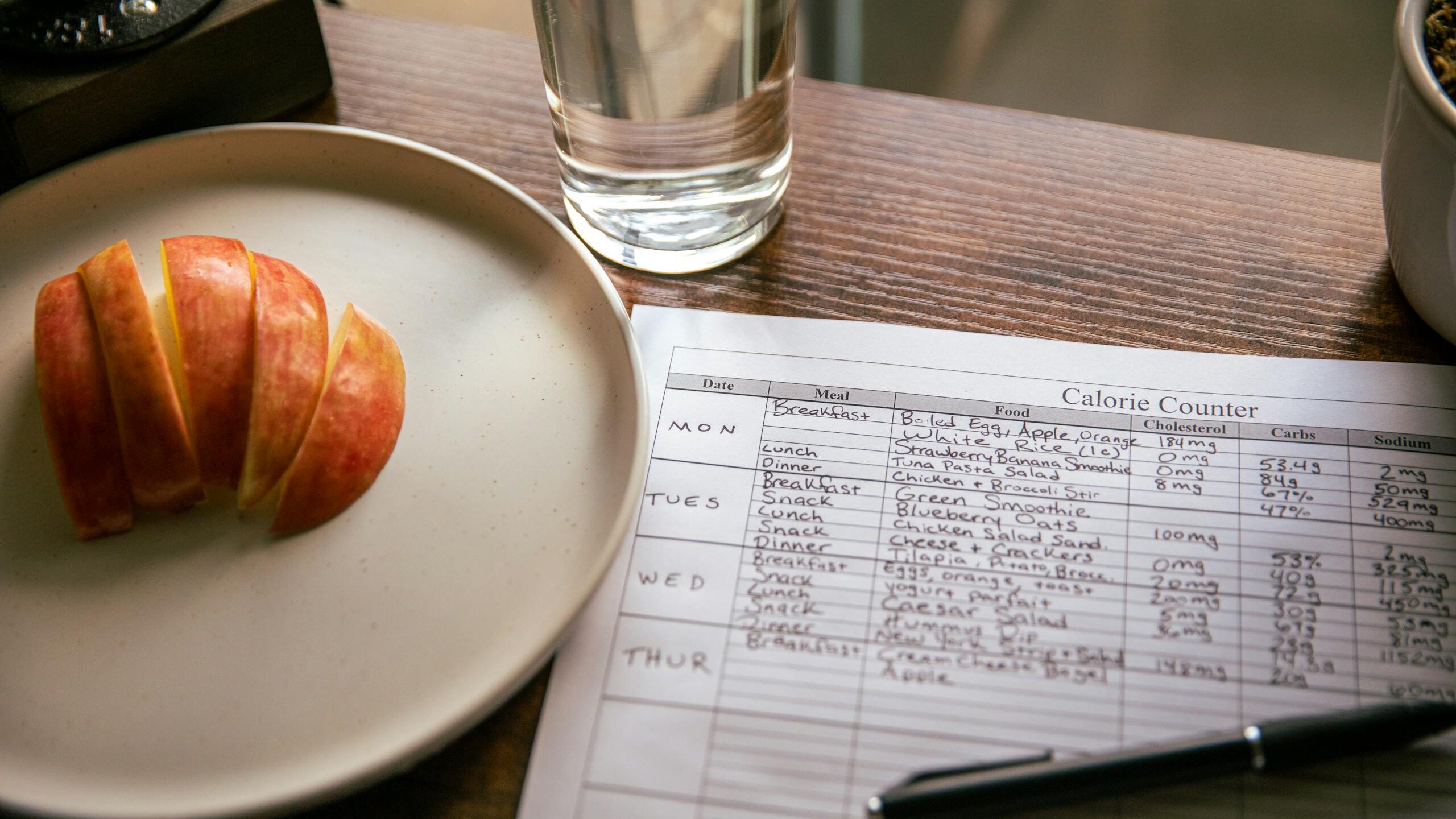 A table setup with apple slices, a calorie counting sheet, and a glass of water for a dieting scene.